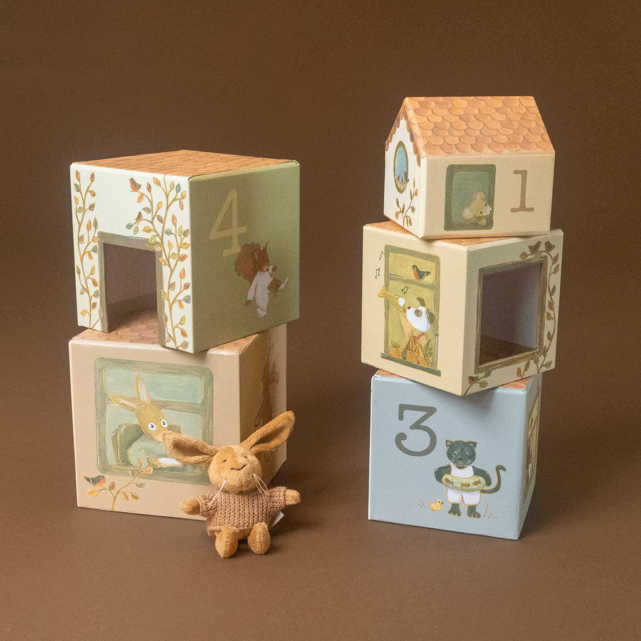 woodland-friends-nesting-blocks-house-lenny-rabbit with animal illustrations, including a house-shaped number 1 block, a number 3 block, a number 4 block, and a small plush rabbit toy, arranged on a brown background.