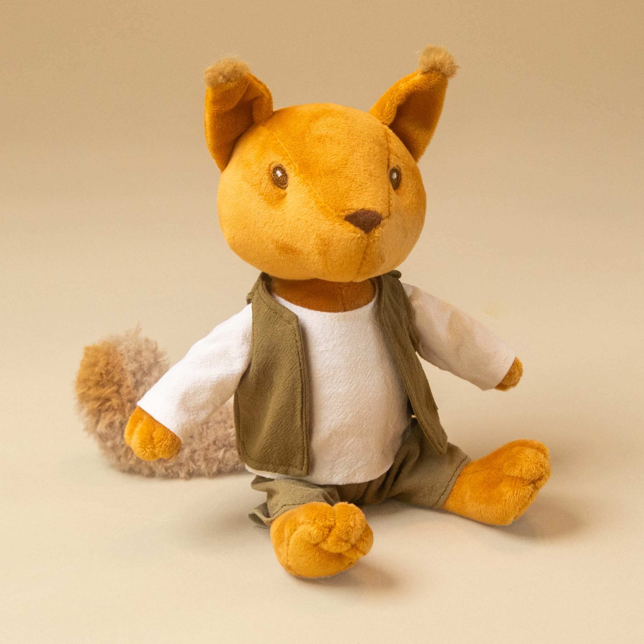 woodland-friends-squirrel-shirt-vest-and-plants sitting upright, wearing a white shirt, olive green vest, and green pants, photographed against a plain warm beige studio background.