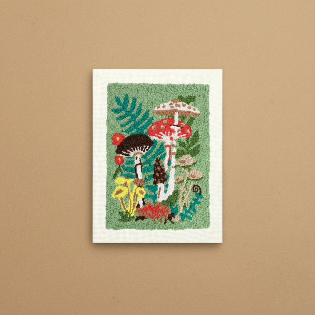 A square wall-hanging or rug-style textile artwork featuring colorful mushrooms and green foliage on a textured light green field, bordered by a white stitched edge, shown against a plain white background.