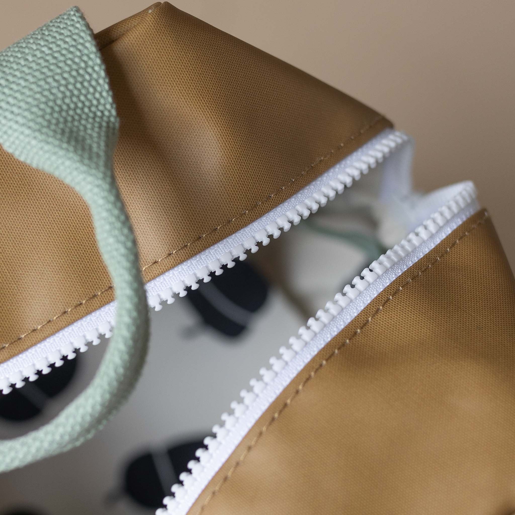 close-up-white-zip-and-green-handle-on-khaki-backpack