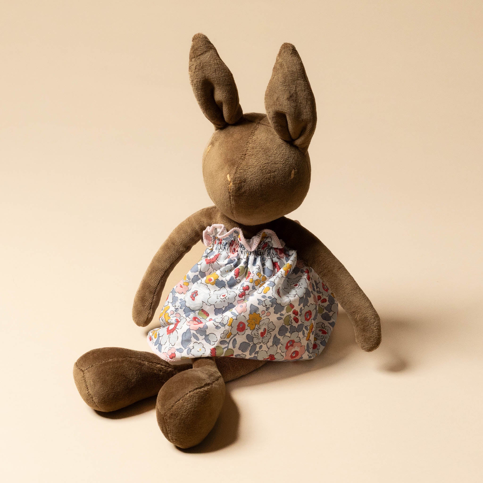 Brown plush bunny with a Grande-Outfit-Liberty-Dress-Grey-_-Blue on a beige background