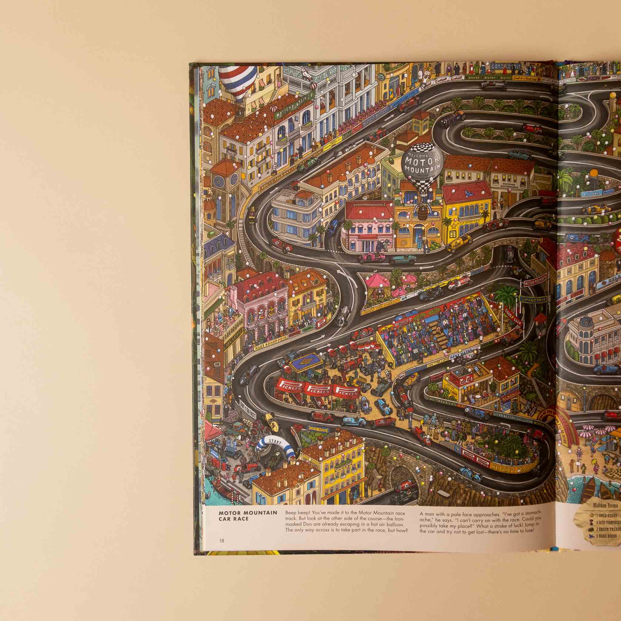 An open book spread showing a highly detailed, colorful illustration of a winding mountain road through a dense town. The left page contains a title reading 'JUGOS MOUNTAIN FOR RACE' and a small caption at the bottom, while the right page is filled with the intricate map-style artwork.