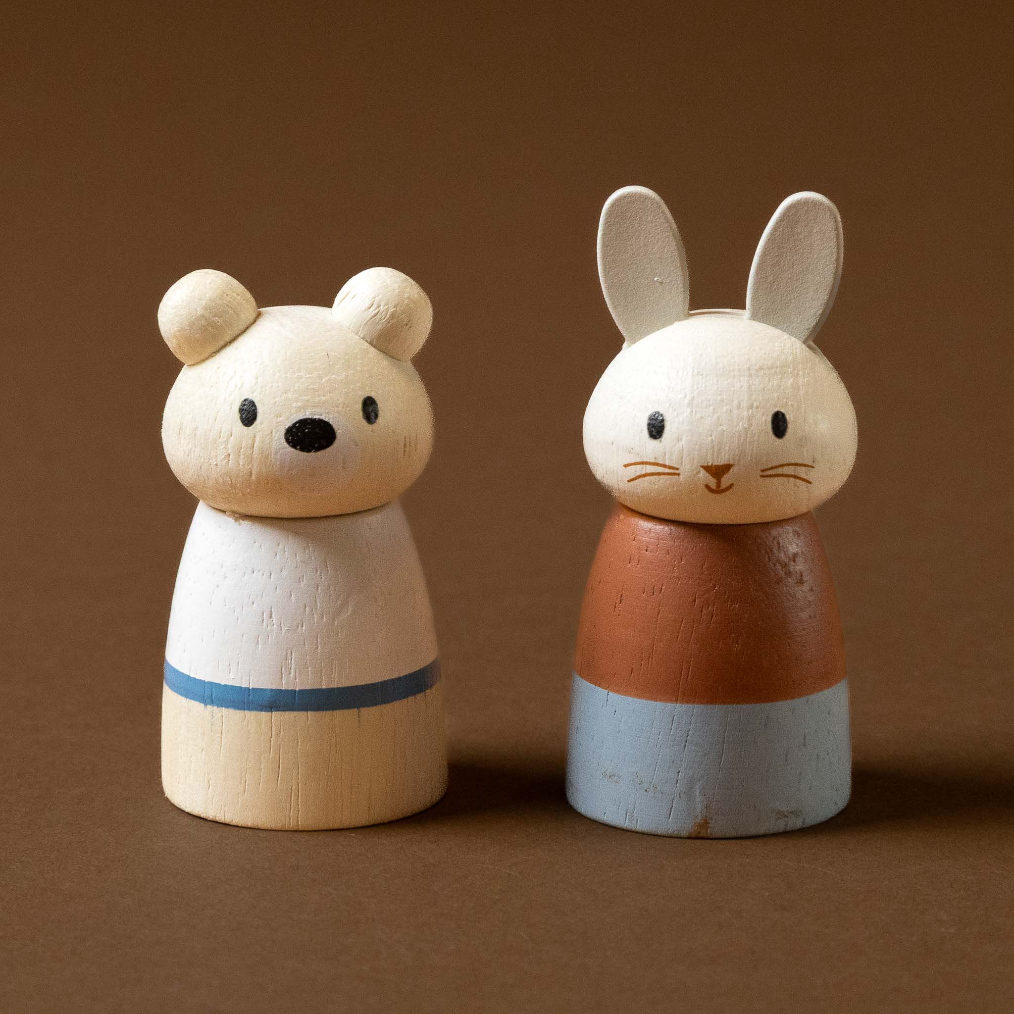 Two wooden animal figurines, one resembling a bear and the other a rabbit, on a brown background.