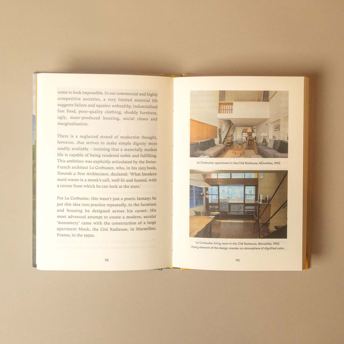 An open book showing two printed interior design pages with text and small architectural photographs, photographed against a plain beige background.