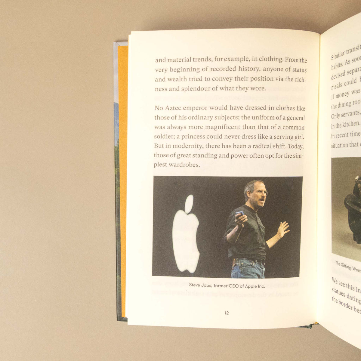 An open book showing printed text and a black-and-white photo of Steve Jobs with the Apple logo, photographed against a plain beige background.