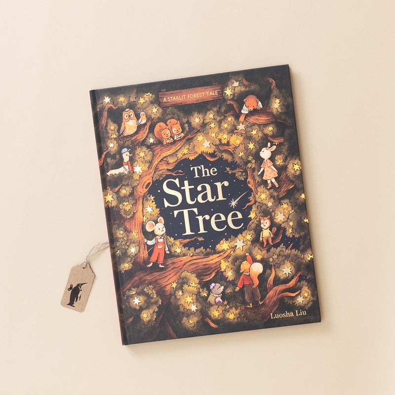 A hardcover children's book titled "The Star Tree" by Luocha Liu, featuring a whimsical cover illustration of forest animals gathered around glowing stars. The book is photographed at an angle on a warm cream background with a small paper bookmark tag attached.