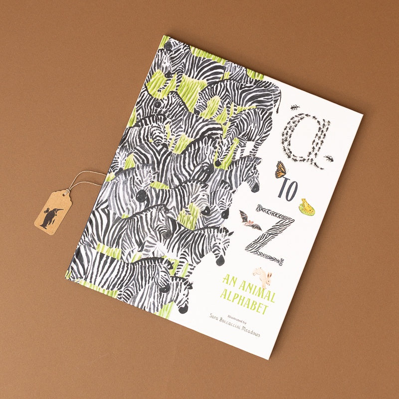 An animal alphabet book titled 'A to Z: An Animal Alphabet' by Sara Bernstein-Brüchmann, featuring a white cover decorated with black-and-white zebras and lime green accents, shown on a brown background with a small paper tag attached.