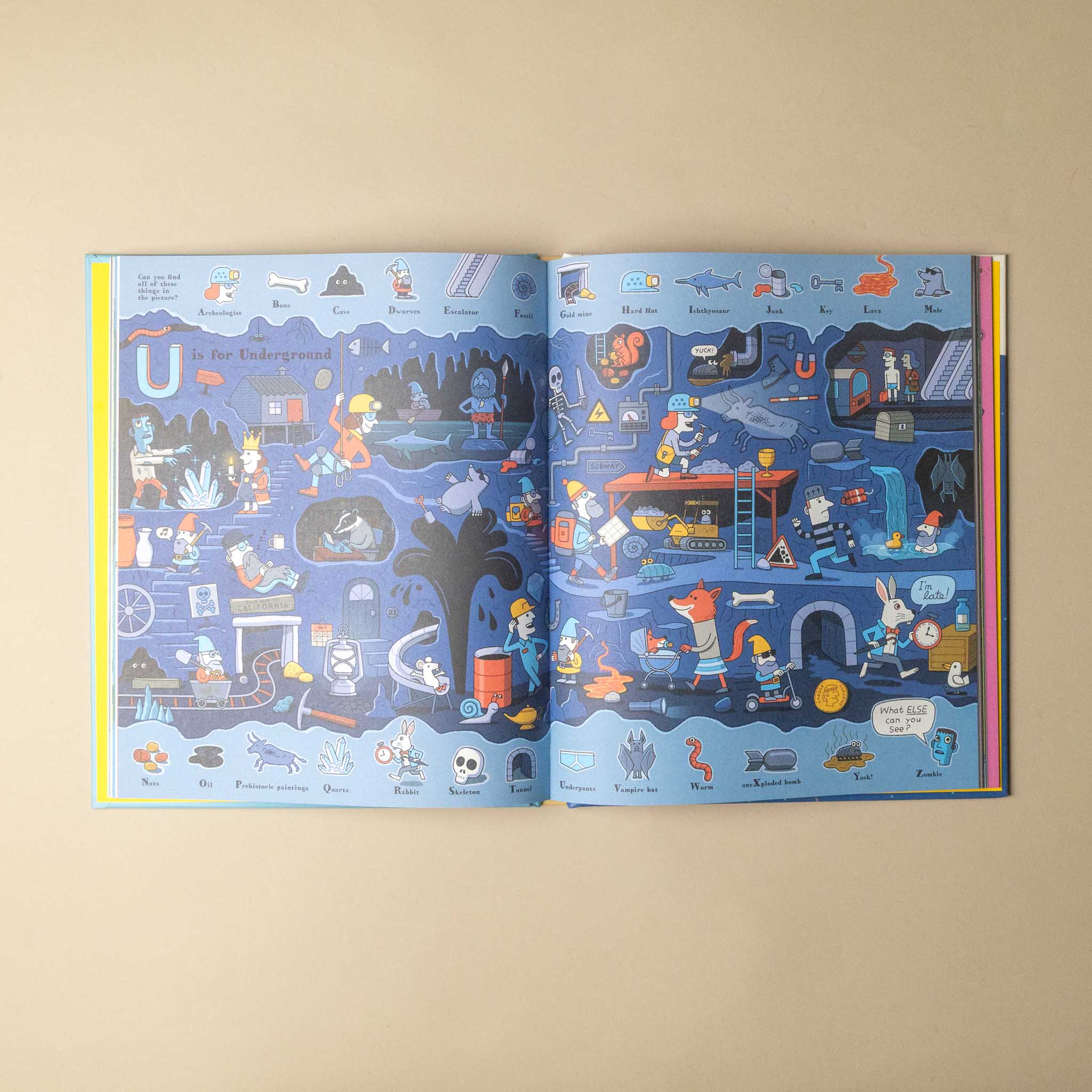 An open illustrated book or magazine spread laid flat on a beige background. The pages are predominantly blue with many small colorful cartoon illustrations and labels, including a large letter U near the top left of the left page.