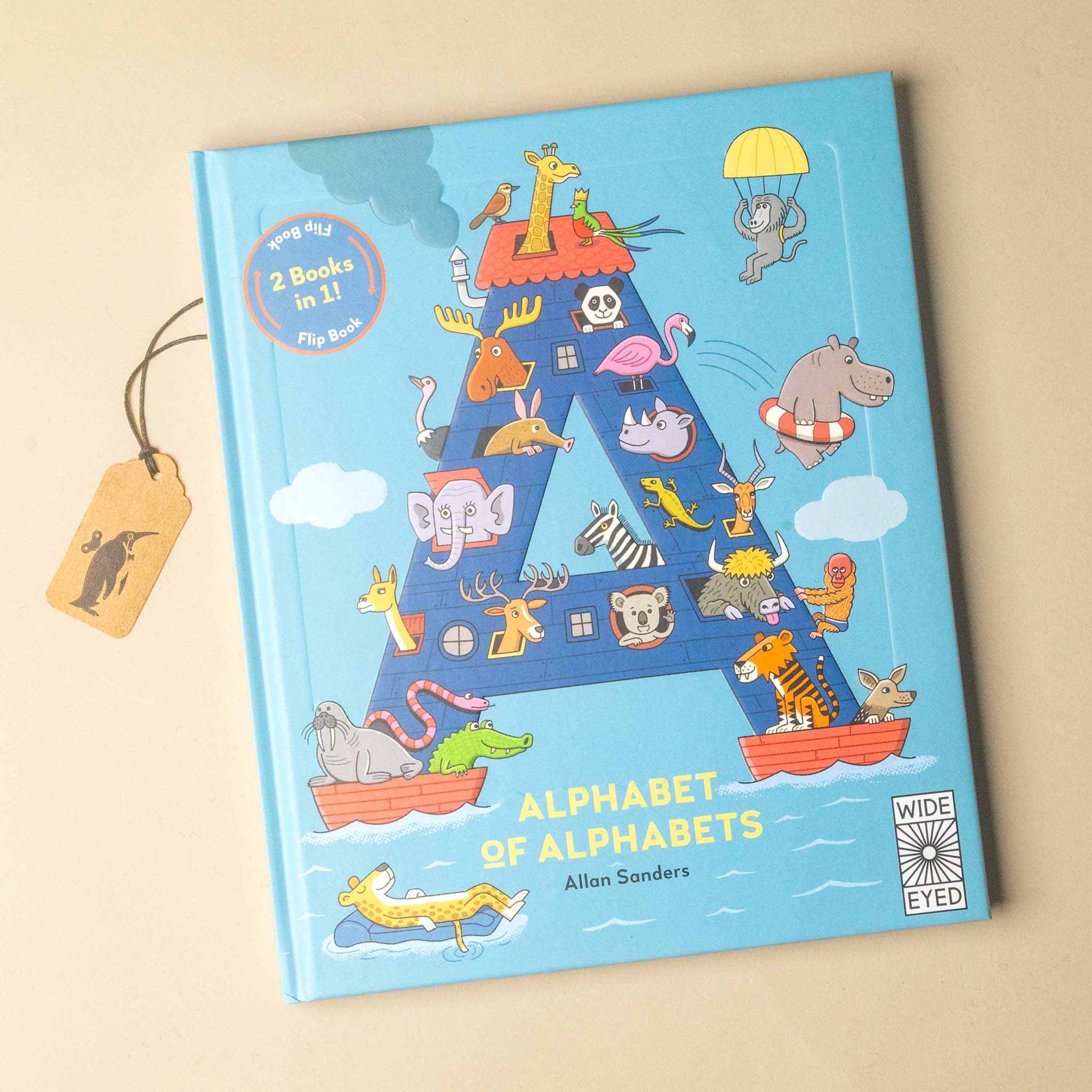 Alphabet of Animals children's book by Alan Sanders, featuring a large blue letter 'A' filled with cartoon animals in small boats on a light blue background. A hanging paper tag is attached to the left side, and the book is photographed on a plain beige surface.