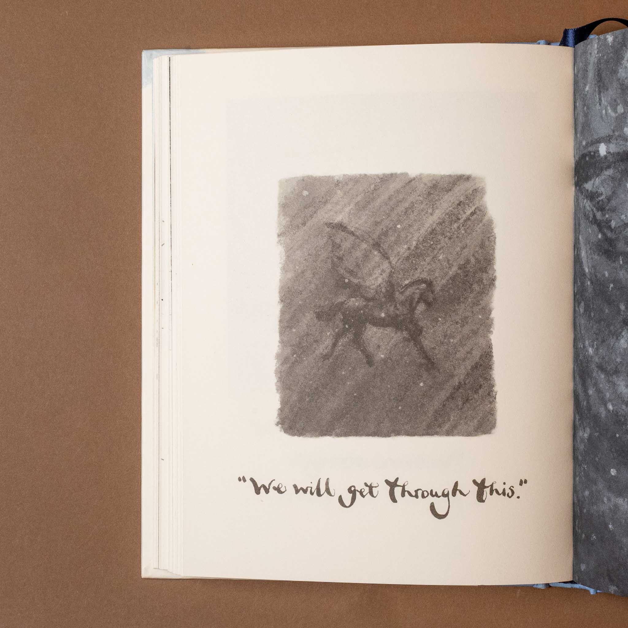 Open always-remember-book with a drawing of a horse with wings and text 'We will get through this' on a brown background.