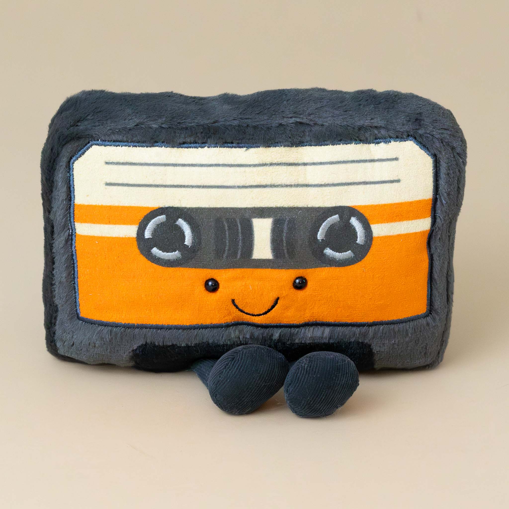 amuseable-cassette-tape-orange-and-white-label-on-black-tape-with-black-feet-stuffed-toy