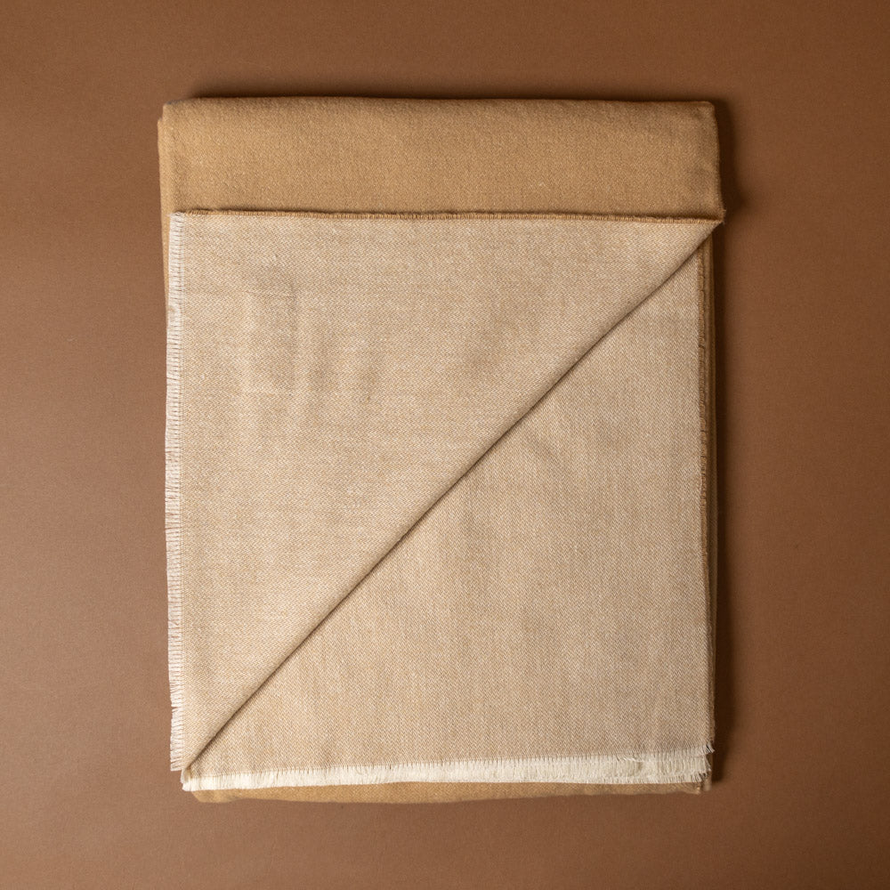aspen-throw-latte Beige fabric folded on a brown background