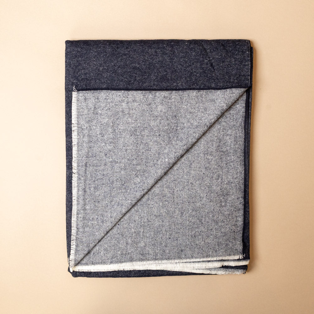 aspen-throw-navy Folded gray and navy blanket on a beige background
