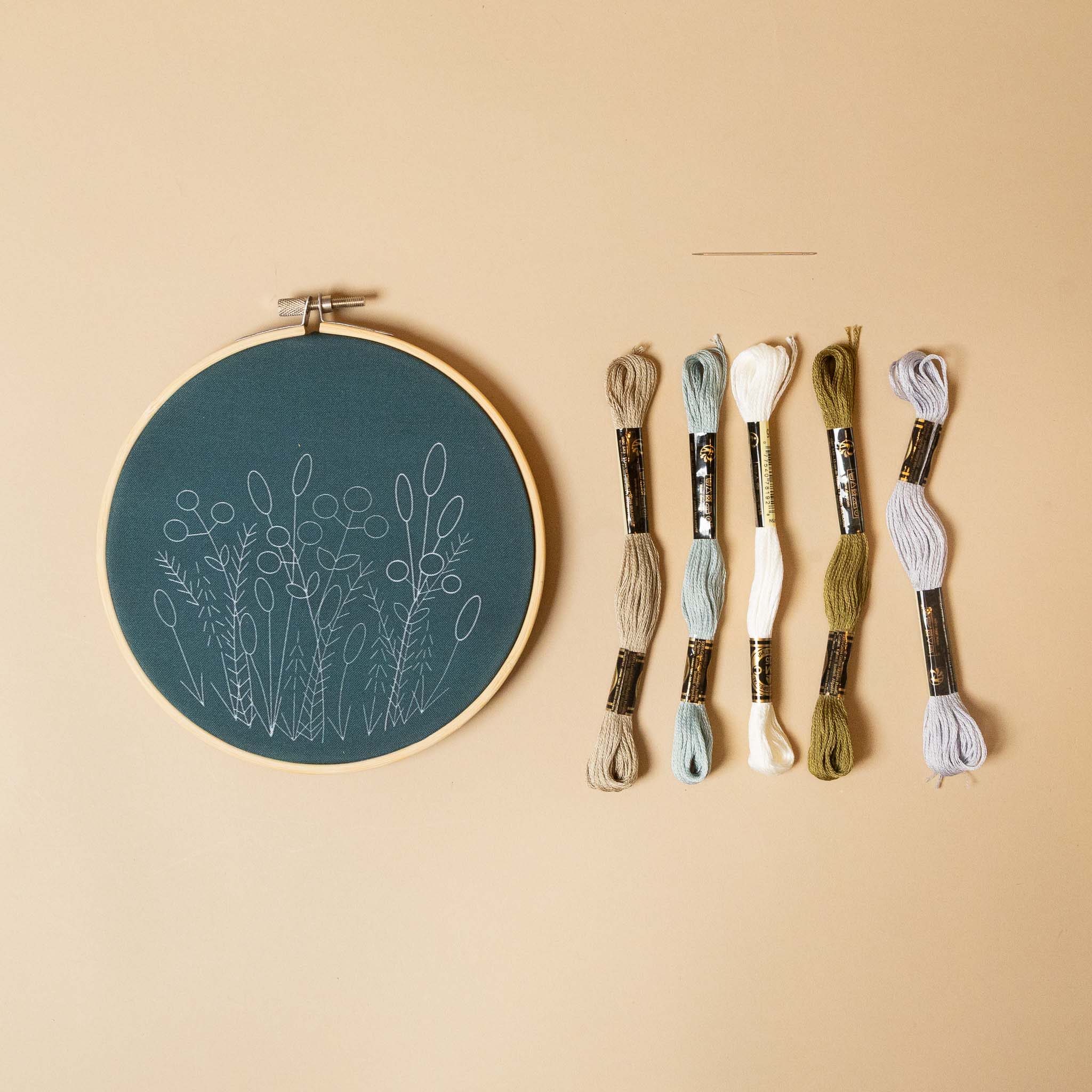avonlea-embroidery-kit-sea-salt embroidery hoop with floral design and set of embroidery threads on a beige background