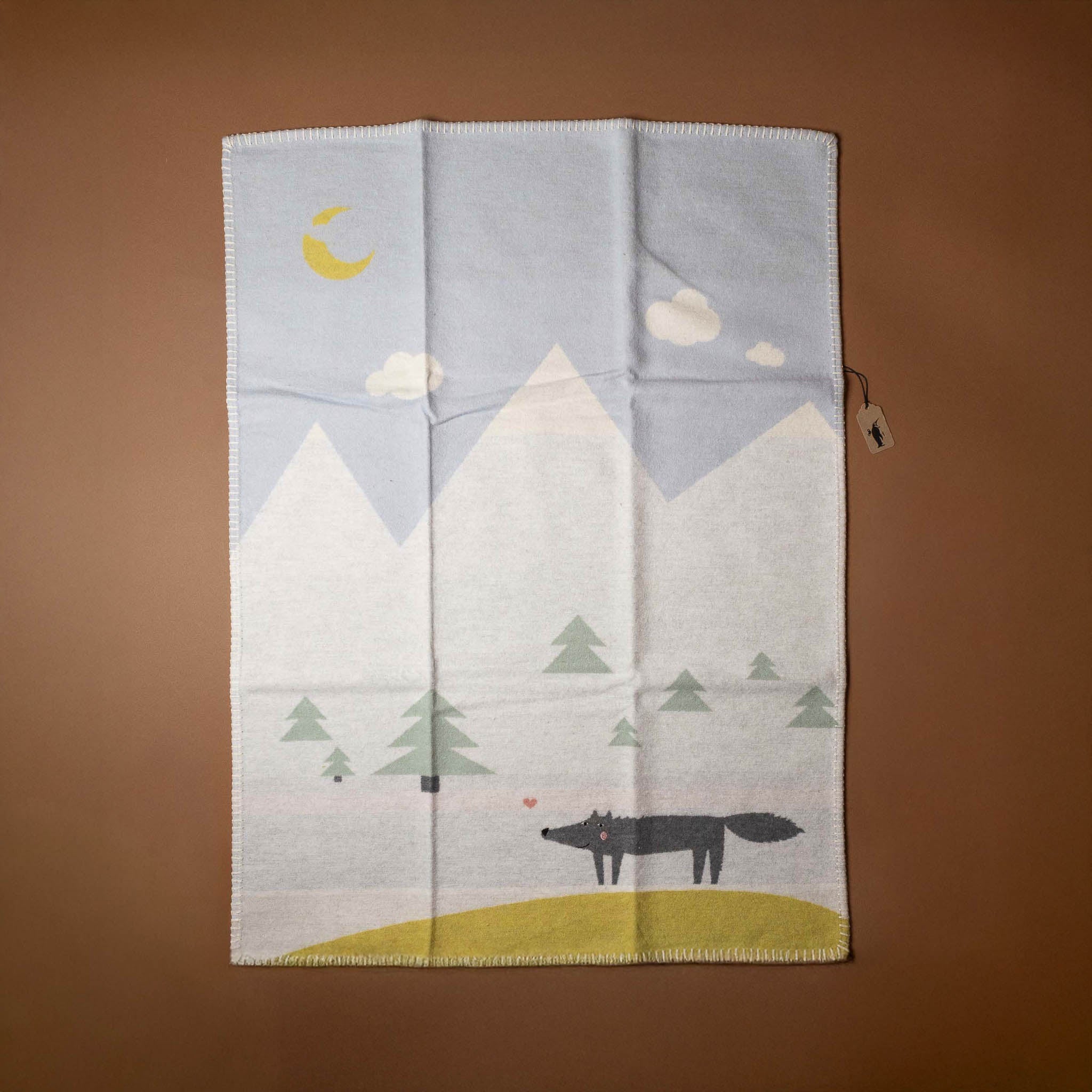 baby-blanket-mountain-wolf Folded blanket with a wolf and mountain design on a brown background