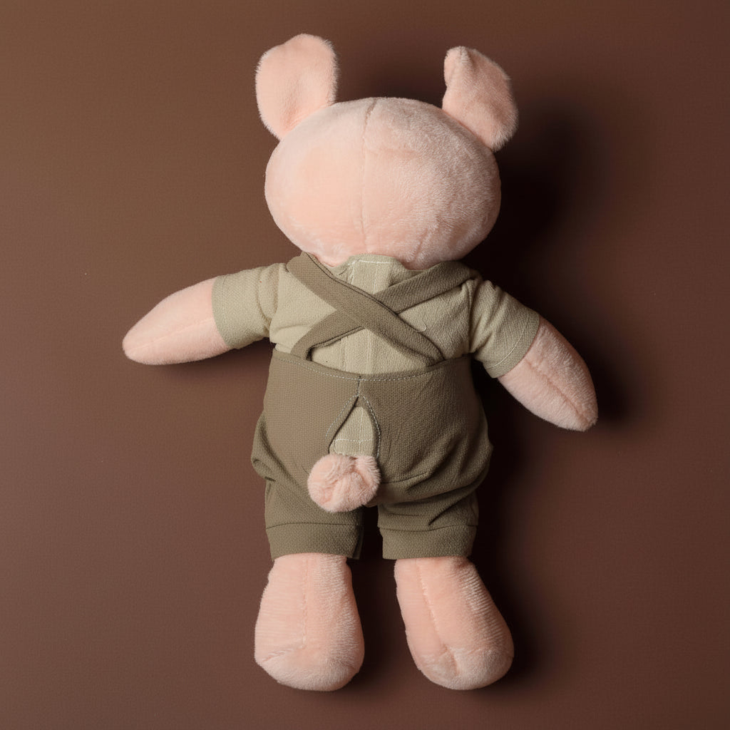 Stuffed  pig toy with pink body and green overalls on a brown background