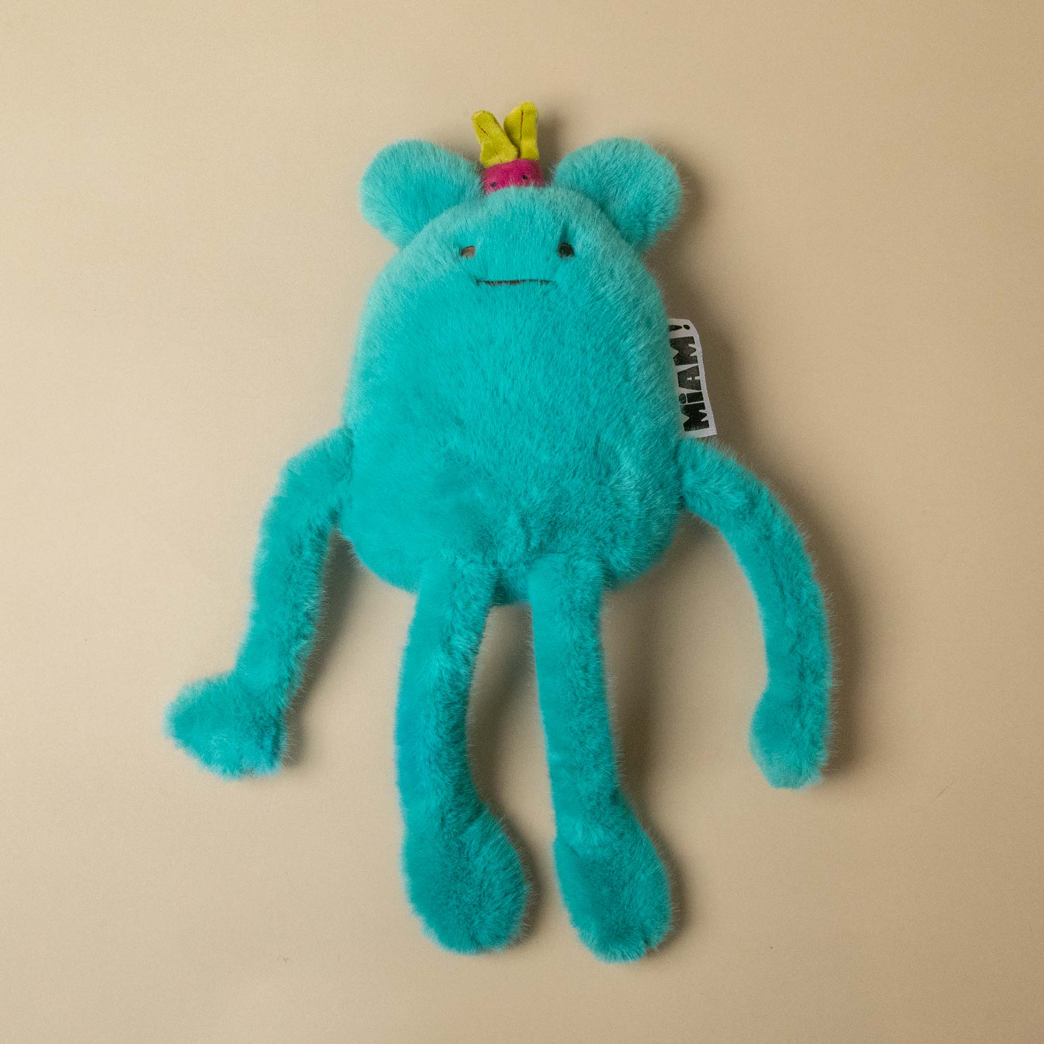 A turquoise blue fuzzy A turquoise blue plush billie-radish-petit toy with long limbs, a small pink flower on its head, and a hangtag, photographed on a plain beige background.plush toy with a small pink and green radish  on its head, sitting on a plain beige background. 