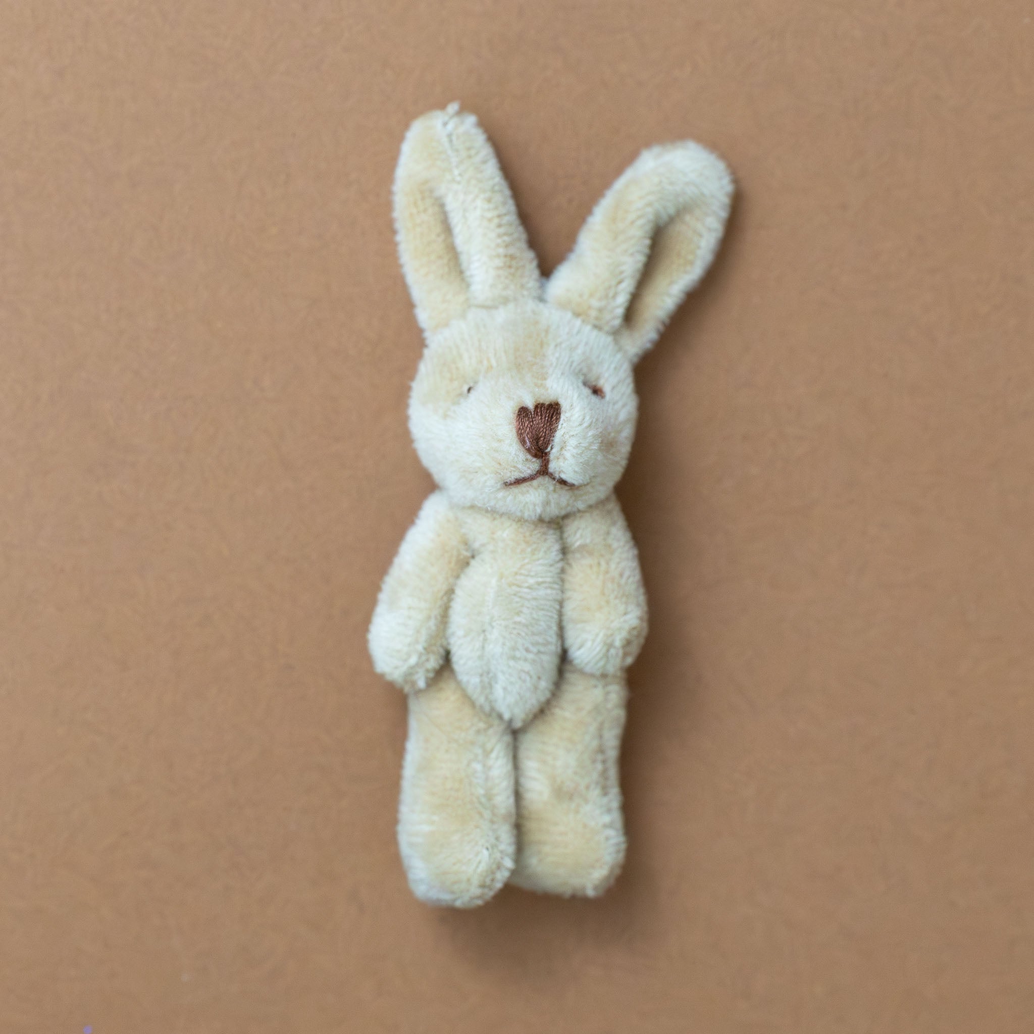 bitty-bunny-oatmeal Small cream-colored stuffed bunny toy on a brown background