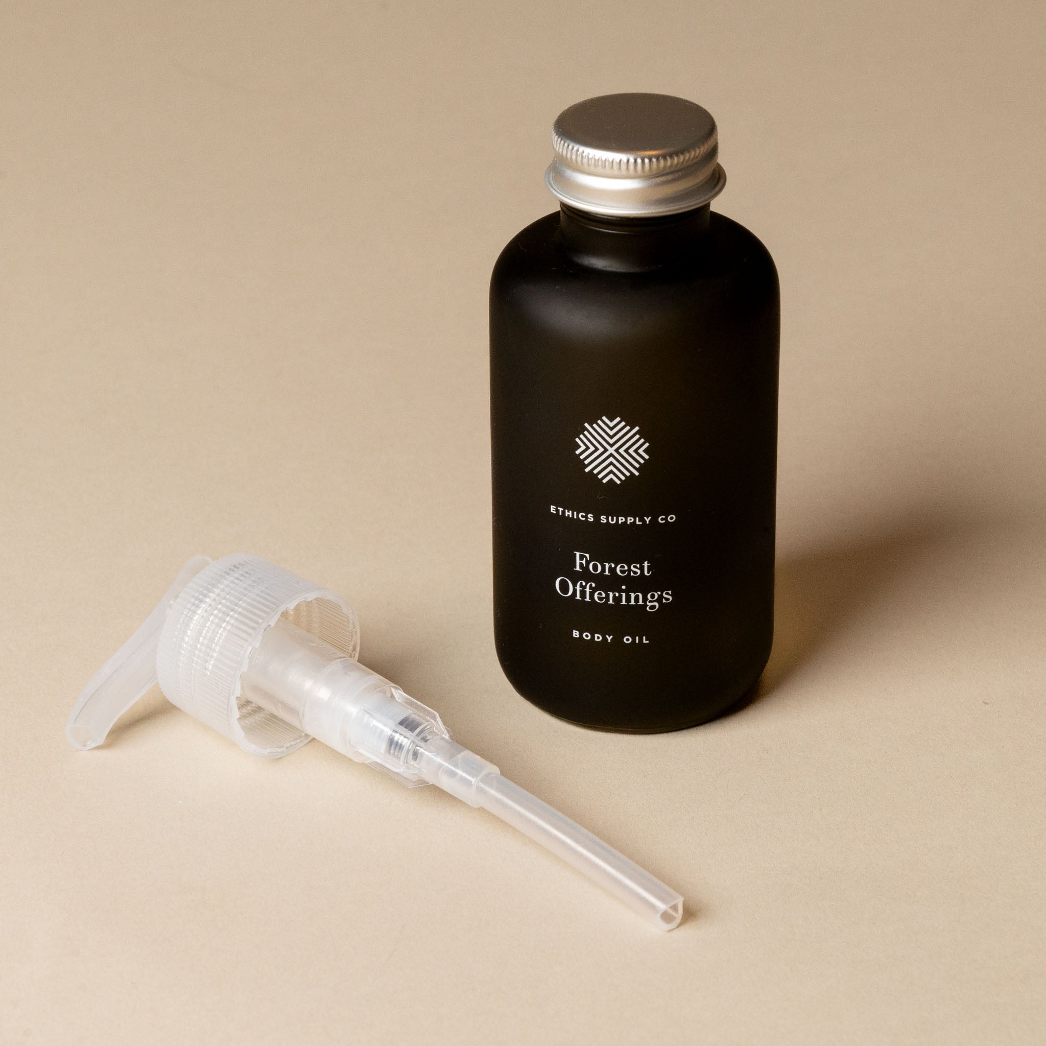 Black bottle of 'Forest Offering' body oil with a silver cap and clear dropper on a beige background.