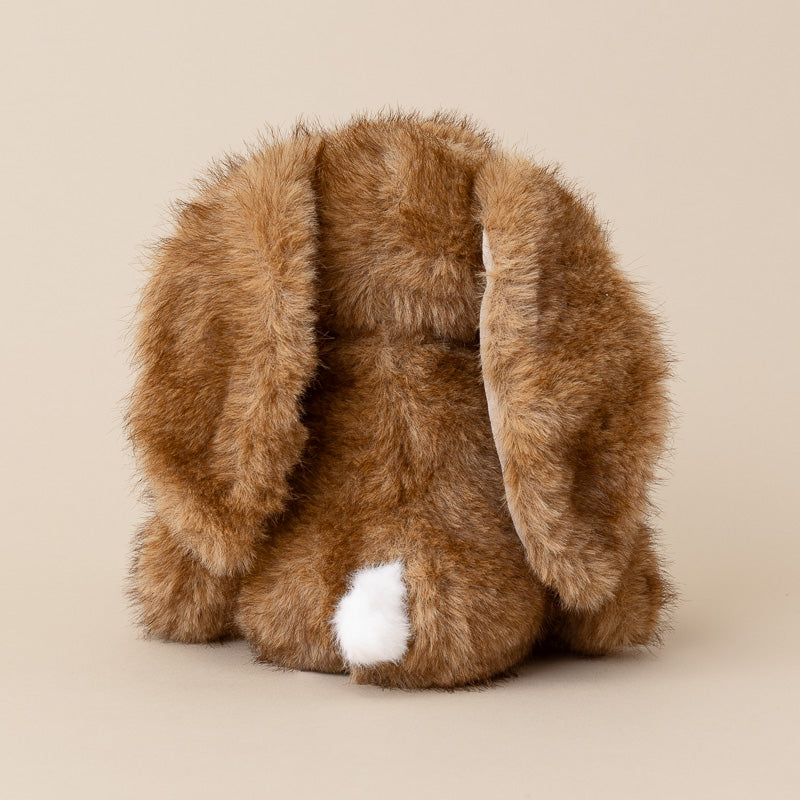 A brown faux fur bunny shown from the back, featuring long floppy ears and a small white tail tip, set against a solid beige background.