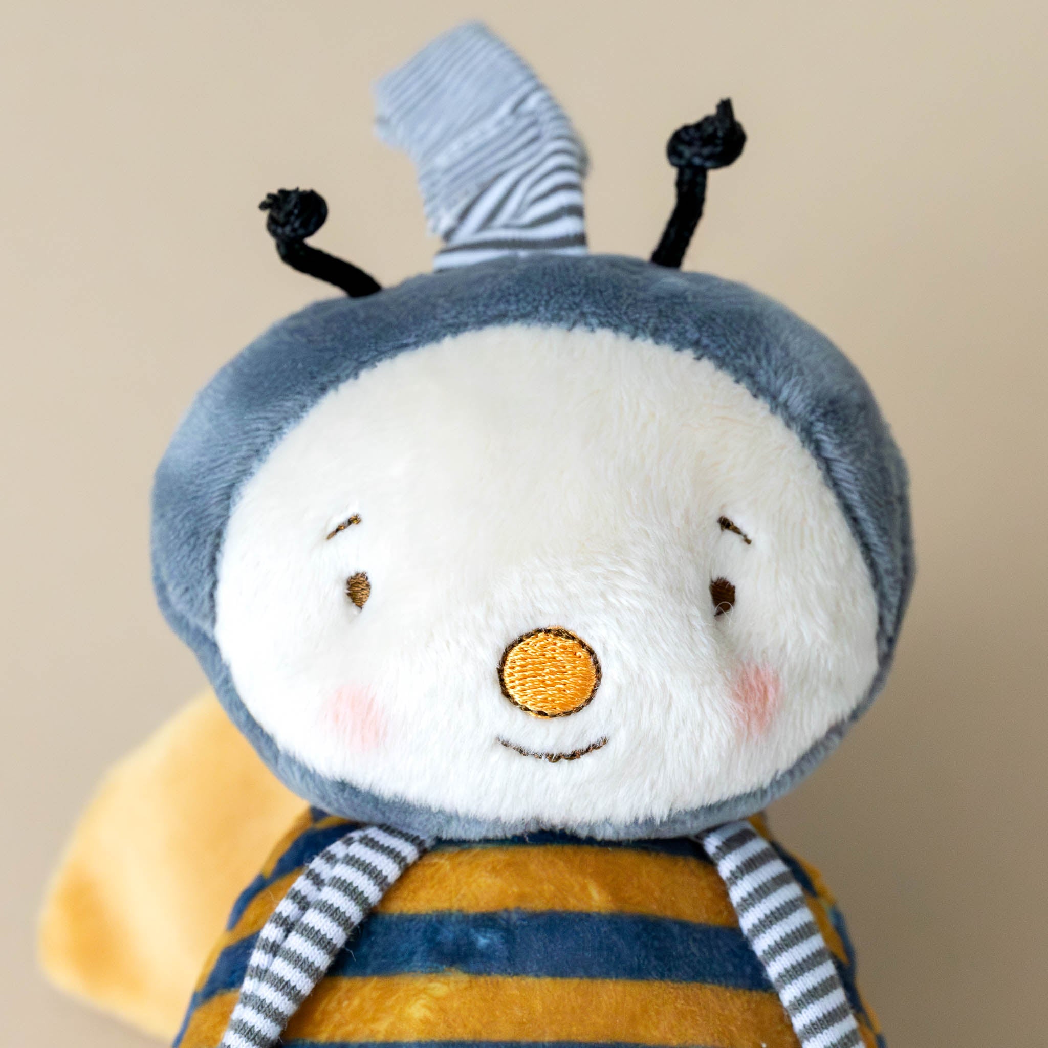 buzzbee-the-bumblebee-stuffed-animal-with-striped-yellow-and-grey-body-grey-cap-black-antenae-ring-for-attaching-to-stroller-and-stiped-legs-rosy-cheeks-yellow-nose-on-cream-face