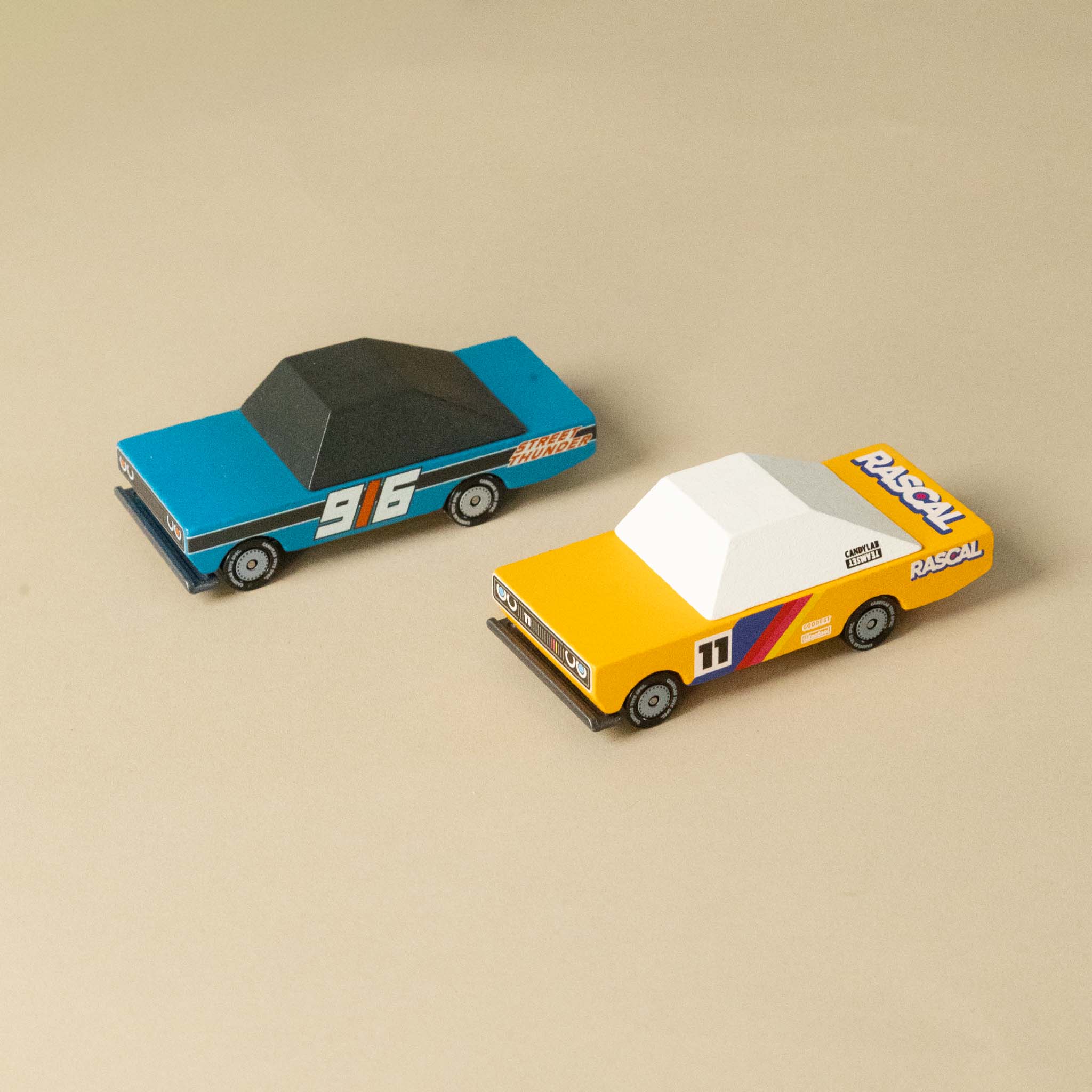candycar-play-set-oval Two toy cars, one blue and one yellow with racing decals, on a beige background