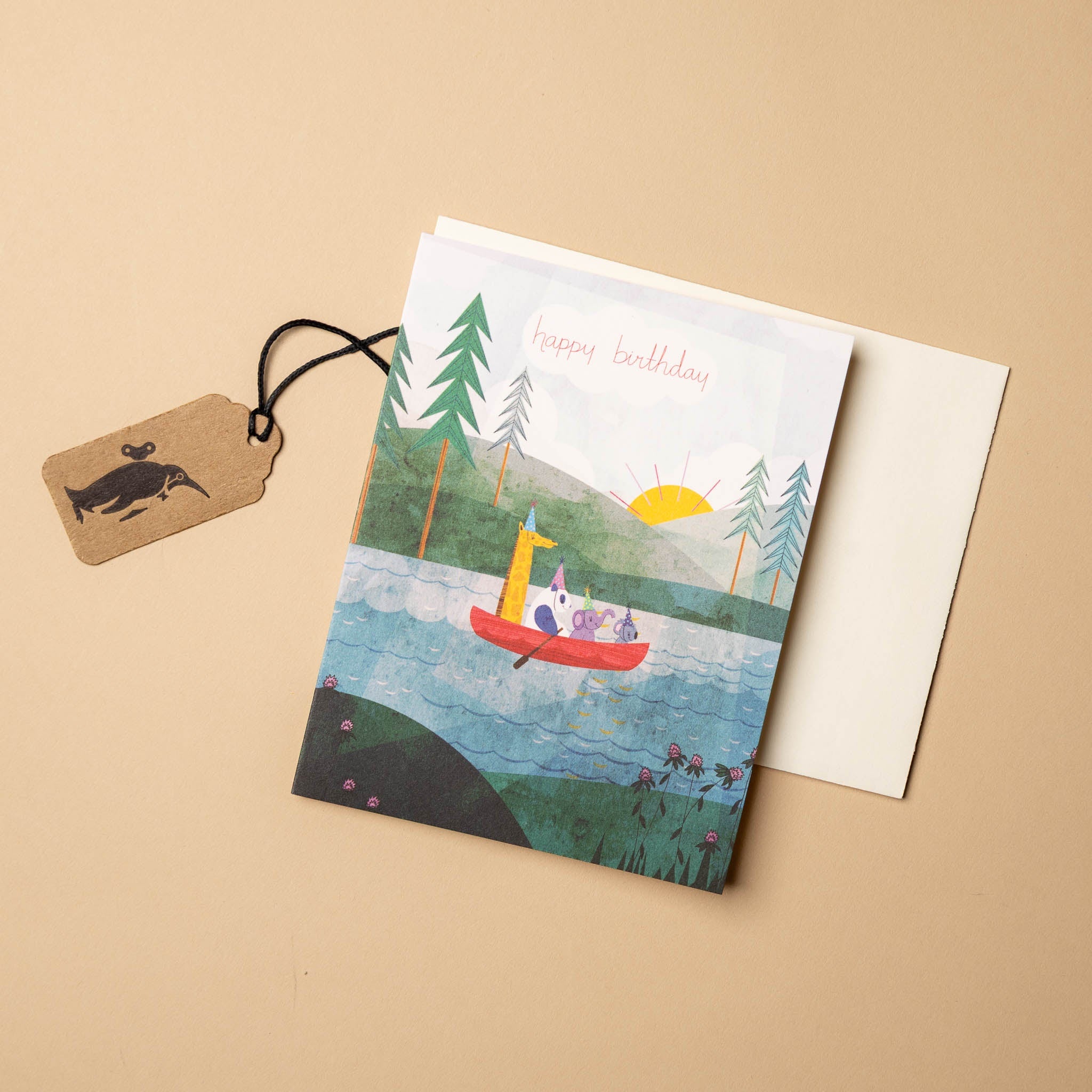Greeting card with a scenic illustration of a lake and boat, accompanied by an envelope and tag on a beige background.