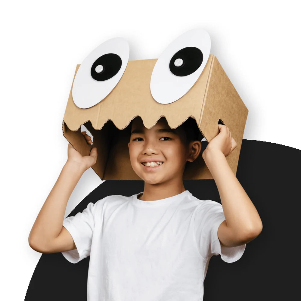 Child wearing a cardboard box costume with googly eyes on a white background