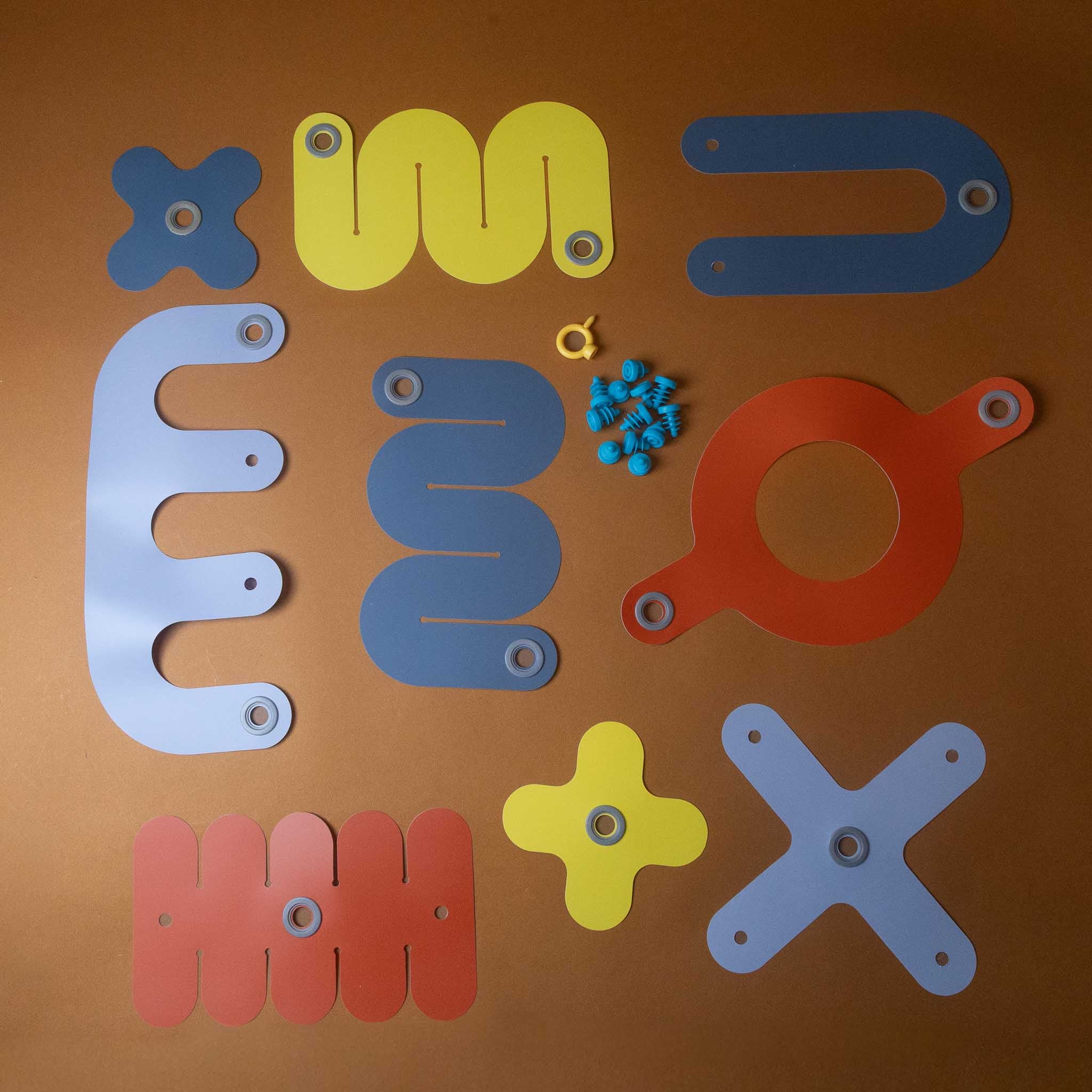A colorful educational pegboard activity set laid out on a brown background, featuring various shaped peg holes in blue, yellow, and red-orange, along with small blue pegs and a small ring.
