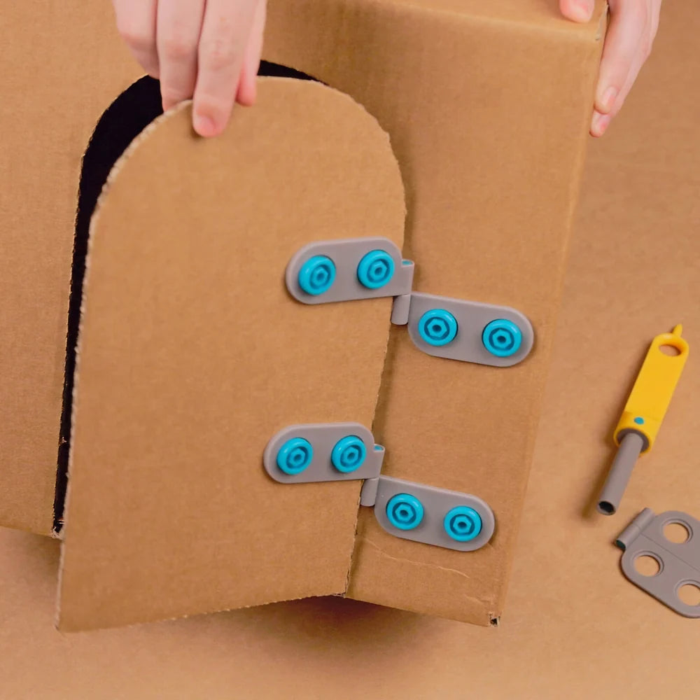 Cardboard door with magnetic strips and hands holding it, with tools on a brown background