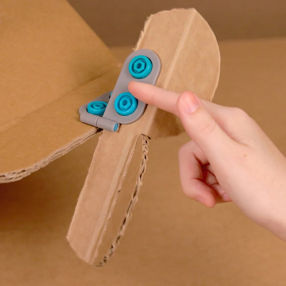 Cardboard object with blue wheels and a hand interacting with it on a brown background