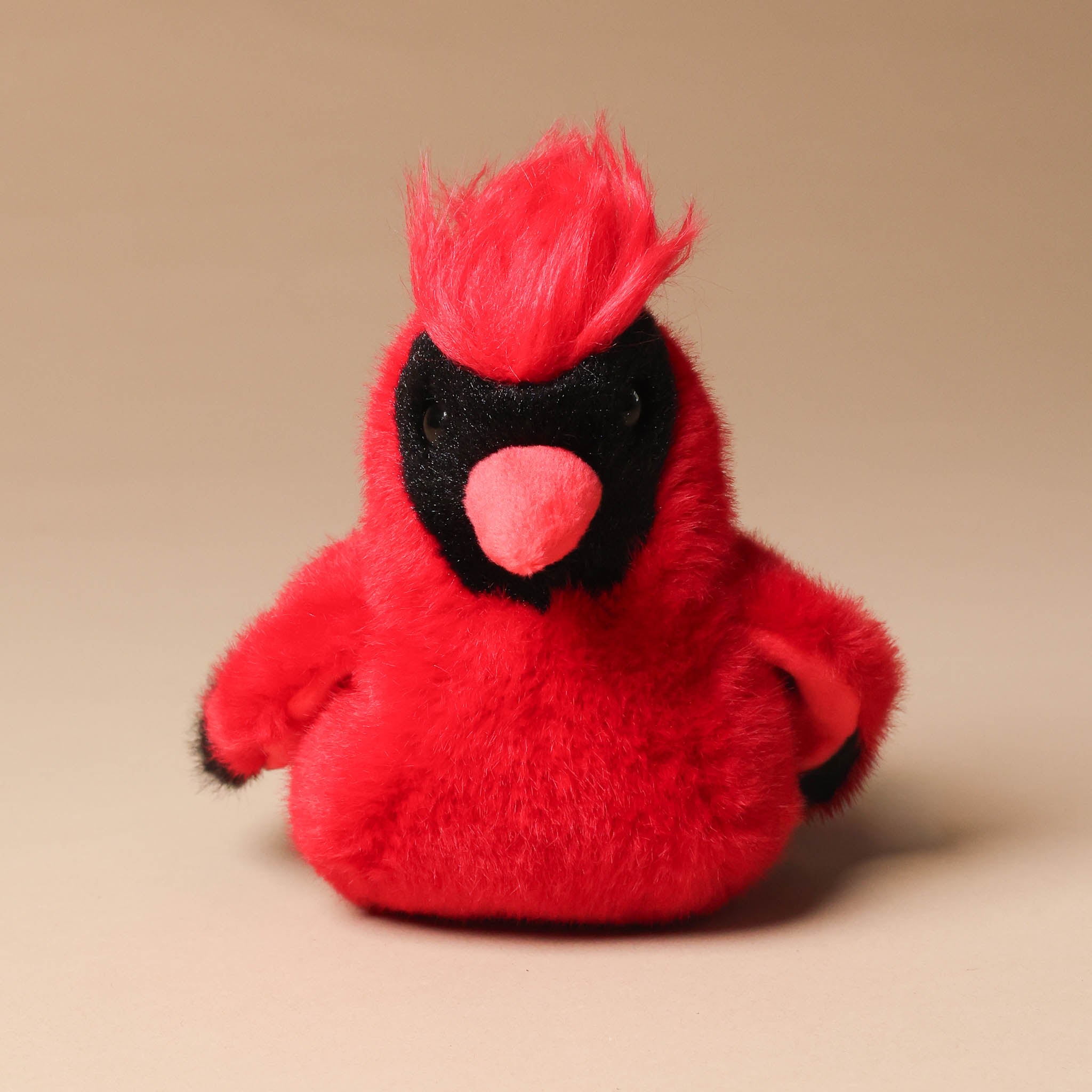 Red plush toy carmine-the-cardinal on a beige background