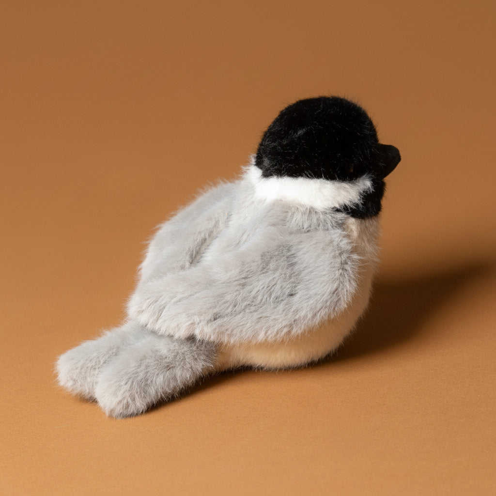Plush toy chipper-the-chicakdee- with a black head and gray body on a brown background