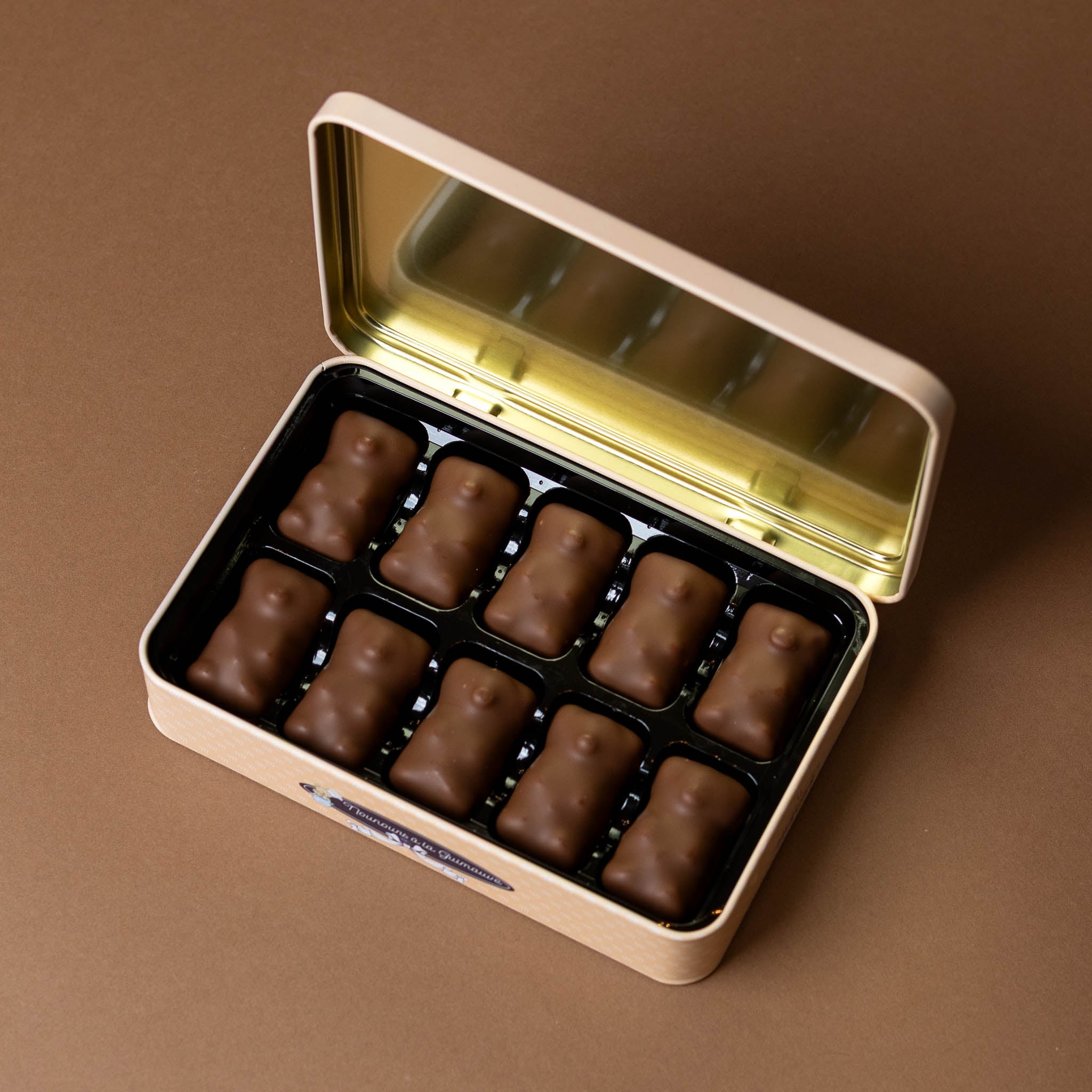 chocolate-covered-marshmallows-in-gift-tin Open gold tin containing chocolate bear candies on a brown background
