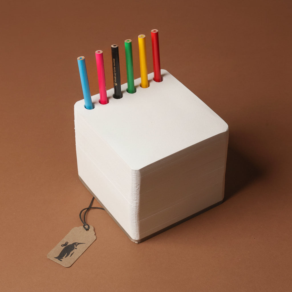 chunky-jotblock-sketch-pad-squared White cube with colorful pencils on a brown background