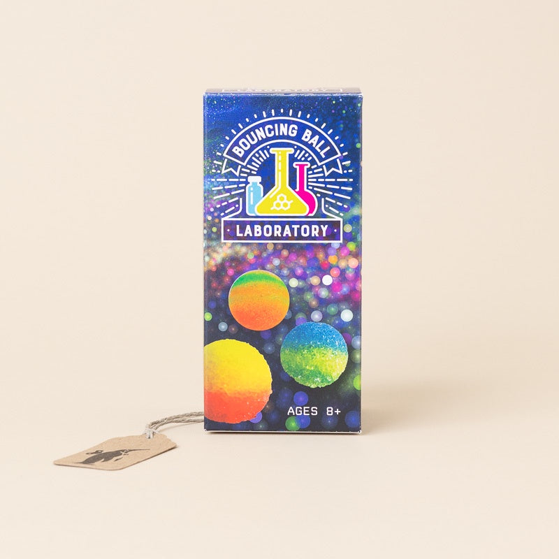 A boxed toy product labeled 'Bouncing Ball Laboratory' with colorful graphics and a small hanging tag, photographed on a plain warm beige background.