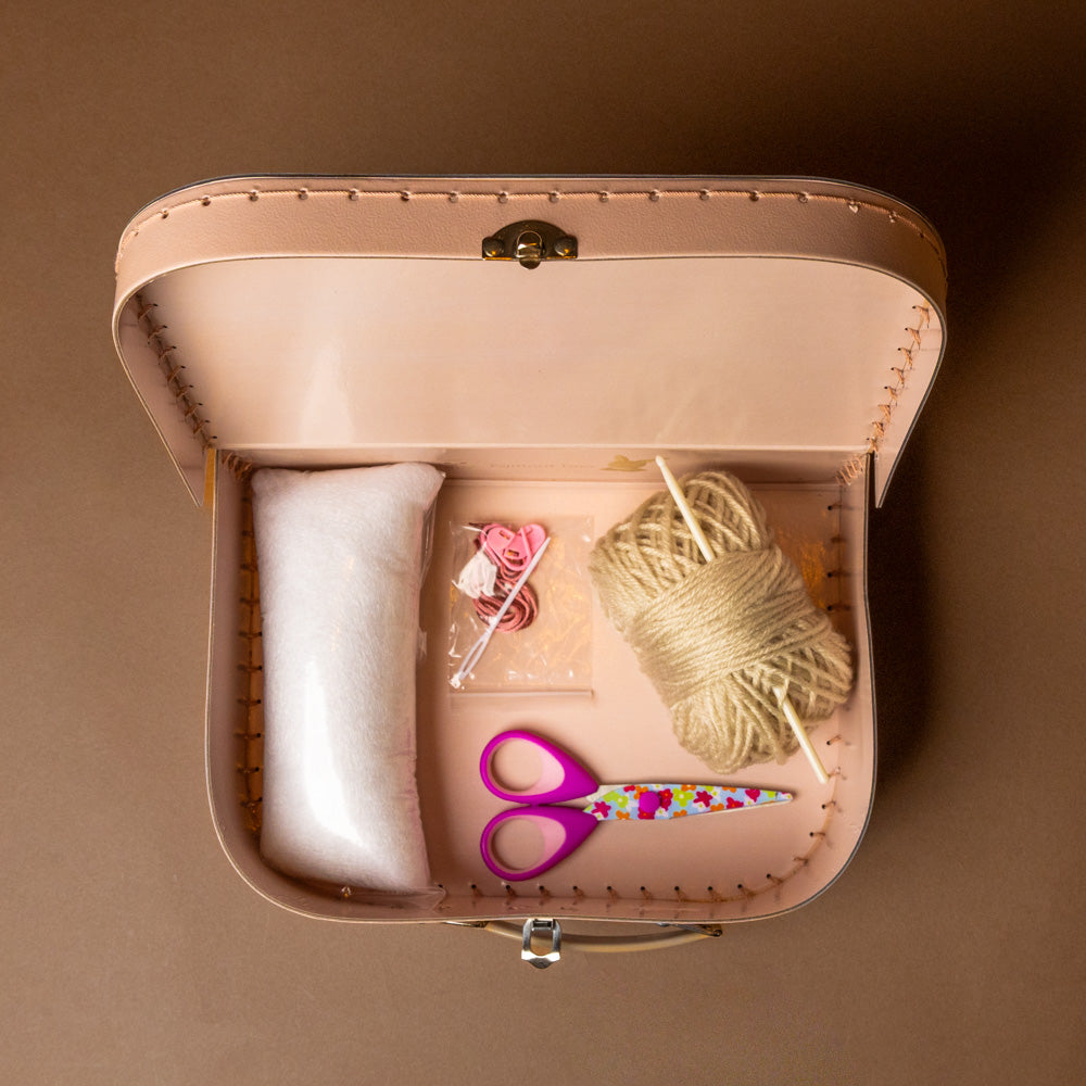 crochet-craft-kit-rabbit Open pink sewing kit with supplies on a brown background