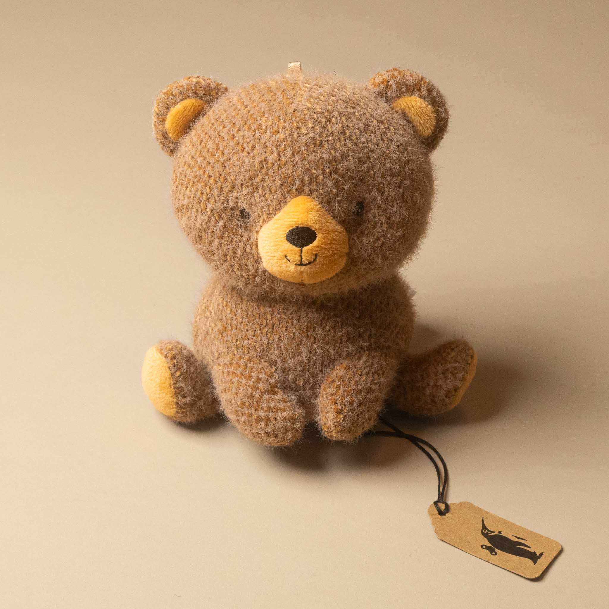 cubby-bear-small plush toy in warm brown with mustard yellow accents on its face, ears, and paws, sitting on a beige background with a small paper tag attached.