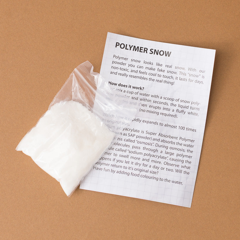 A printed instruction sheet titled 'POLYMER SNOW' lies on a tan background next to a clear plastic bag containing white powder. The sheet explains how to mix the powder with water and describes the expansion effect of the polymer.