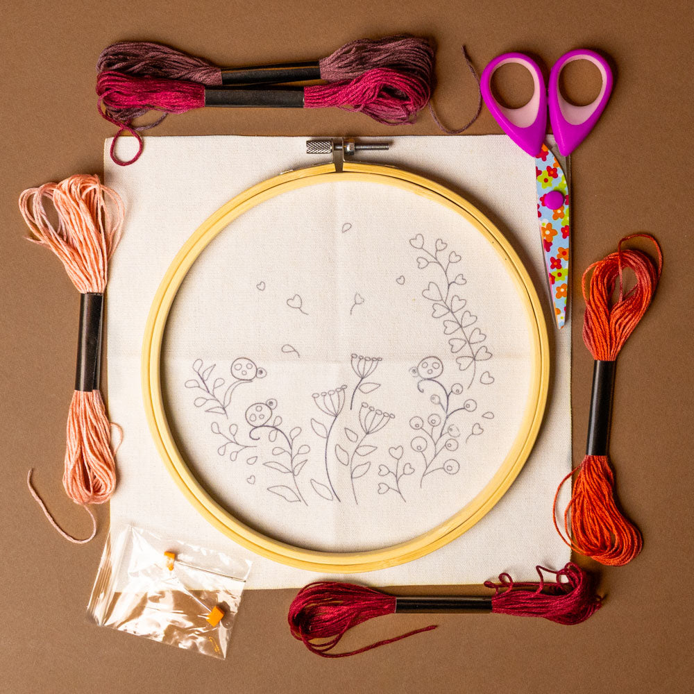 embroidery-craft-kit-ladybugs-and-flowers Embroidery hoop with floral pattern, scissors, and colorful thread on a brown background