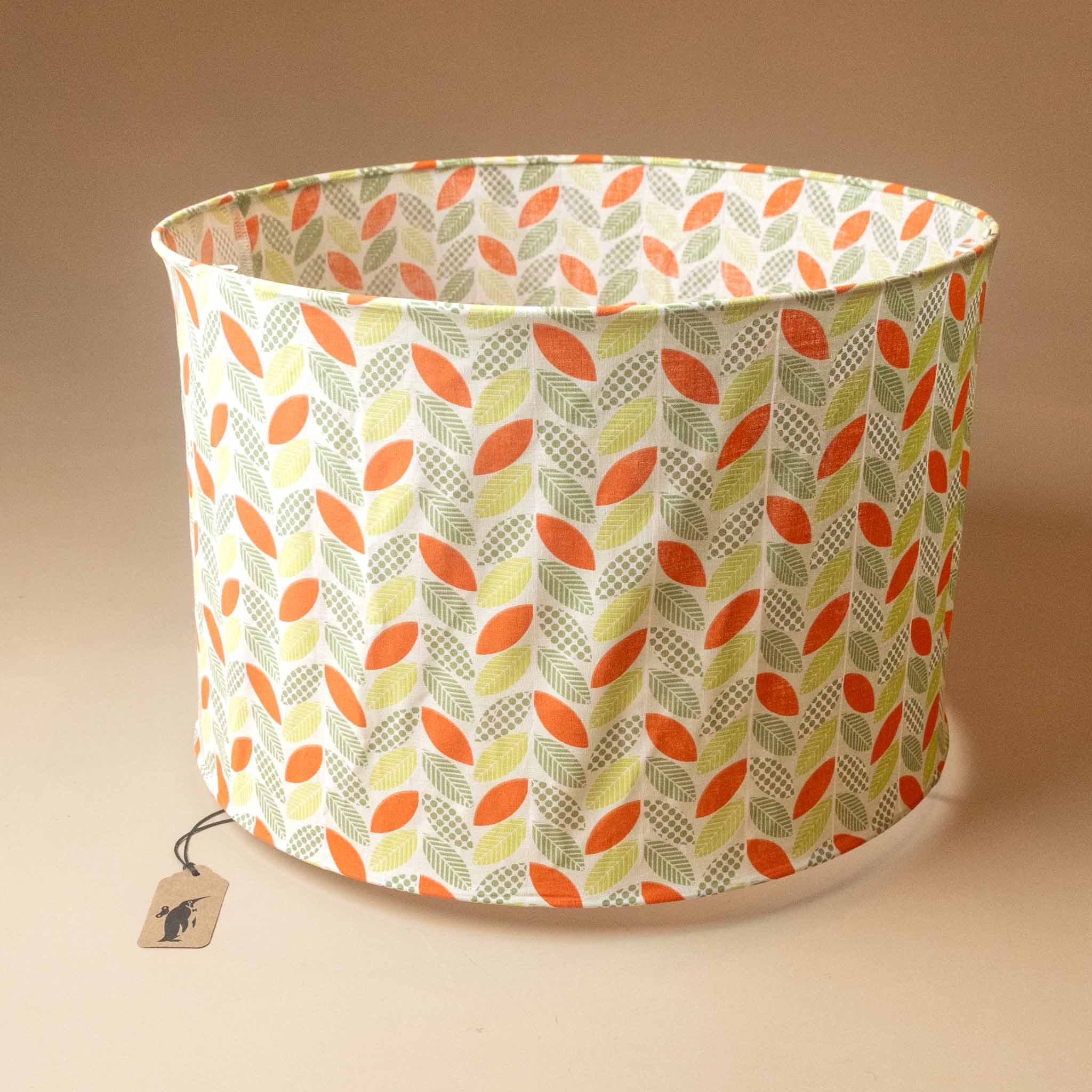 A fabric-lantern-herringbone-leaffeaturing a retro vertical leaf pattern in orange, olive green, and pale yellow on a cream background, shown with a small brand tag.