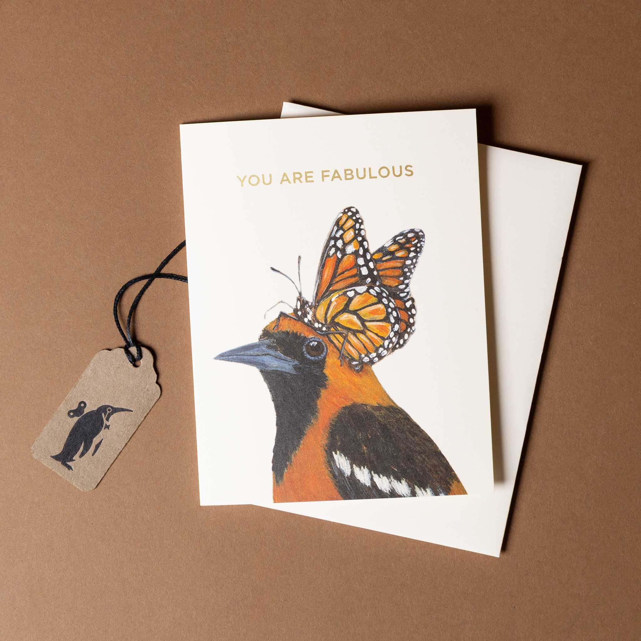 fabulous-oriole-greeting-cardwith a bird and butterfly illustration and a tag on a brown background