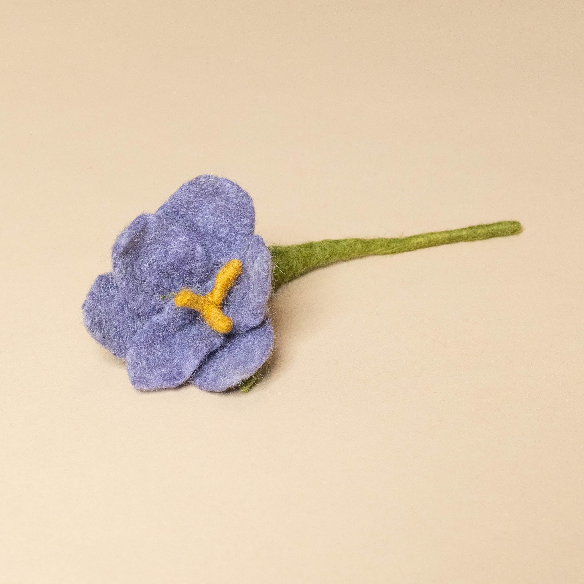 Felted purple flower with a yellow center on a beige background