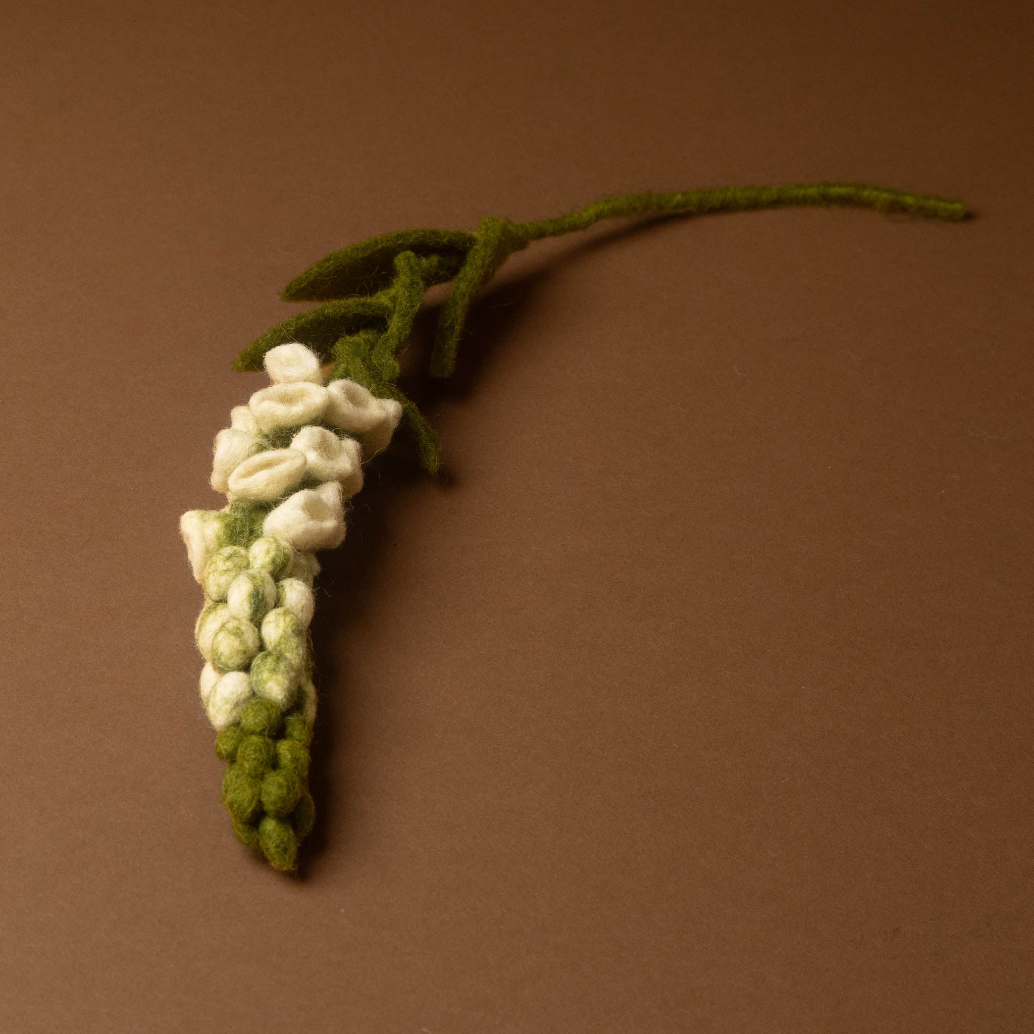 A handcrafted felt-foxglove-flower-white and leaves, displayed on a solid brown background.