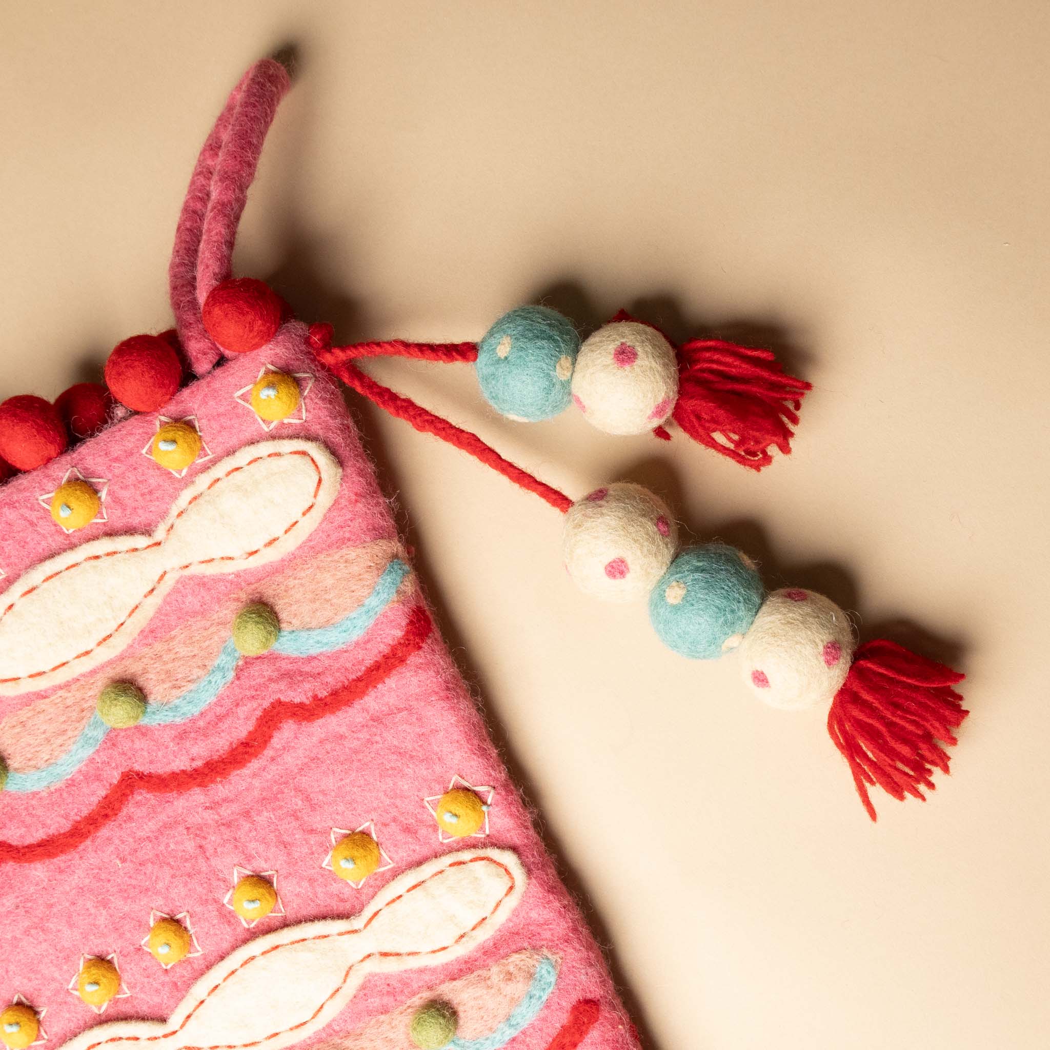 felted-evergreen-stocking-sugar-plum Decorative pink bag with colorful tassels on a beige background