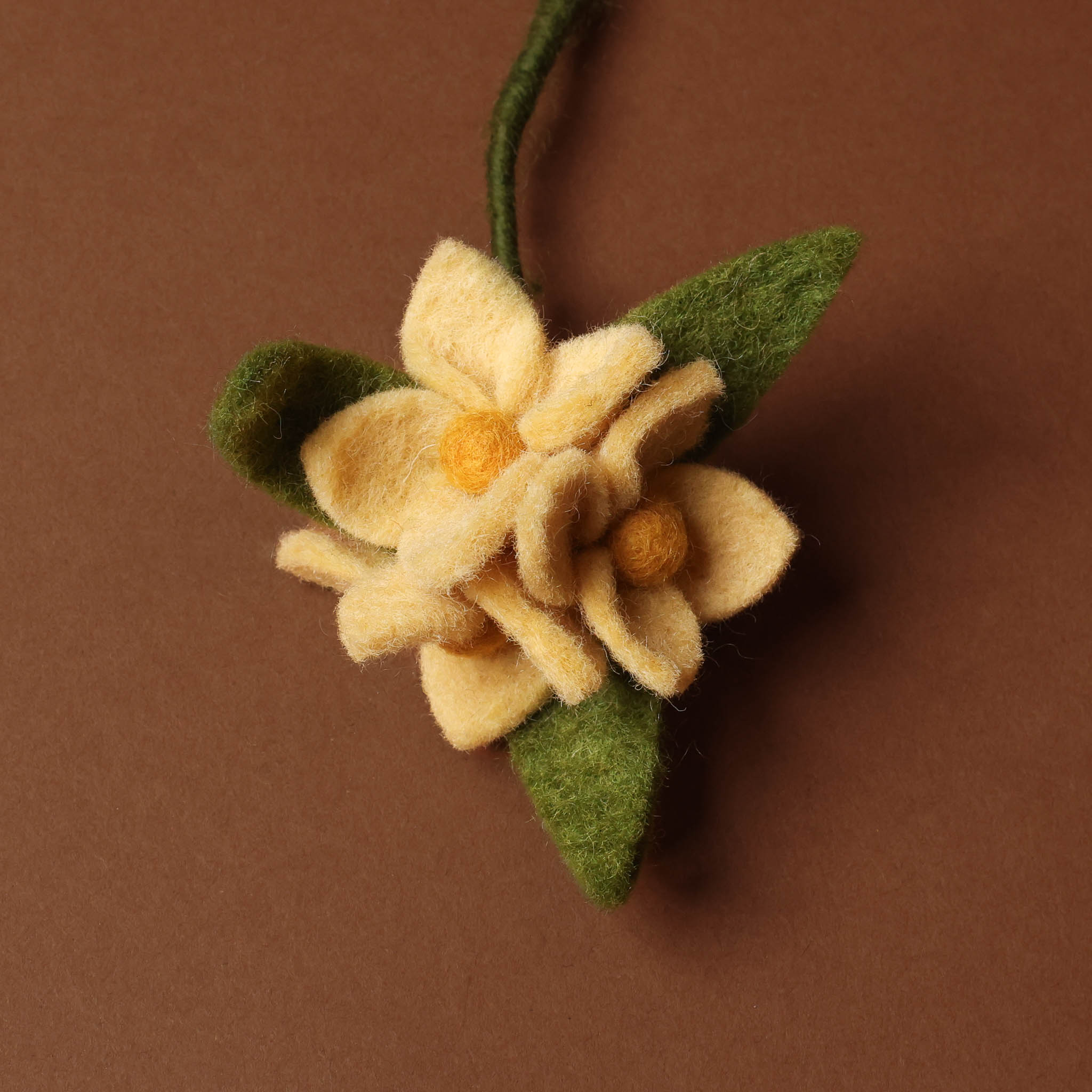 Felted flower with green leaves on a brown background