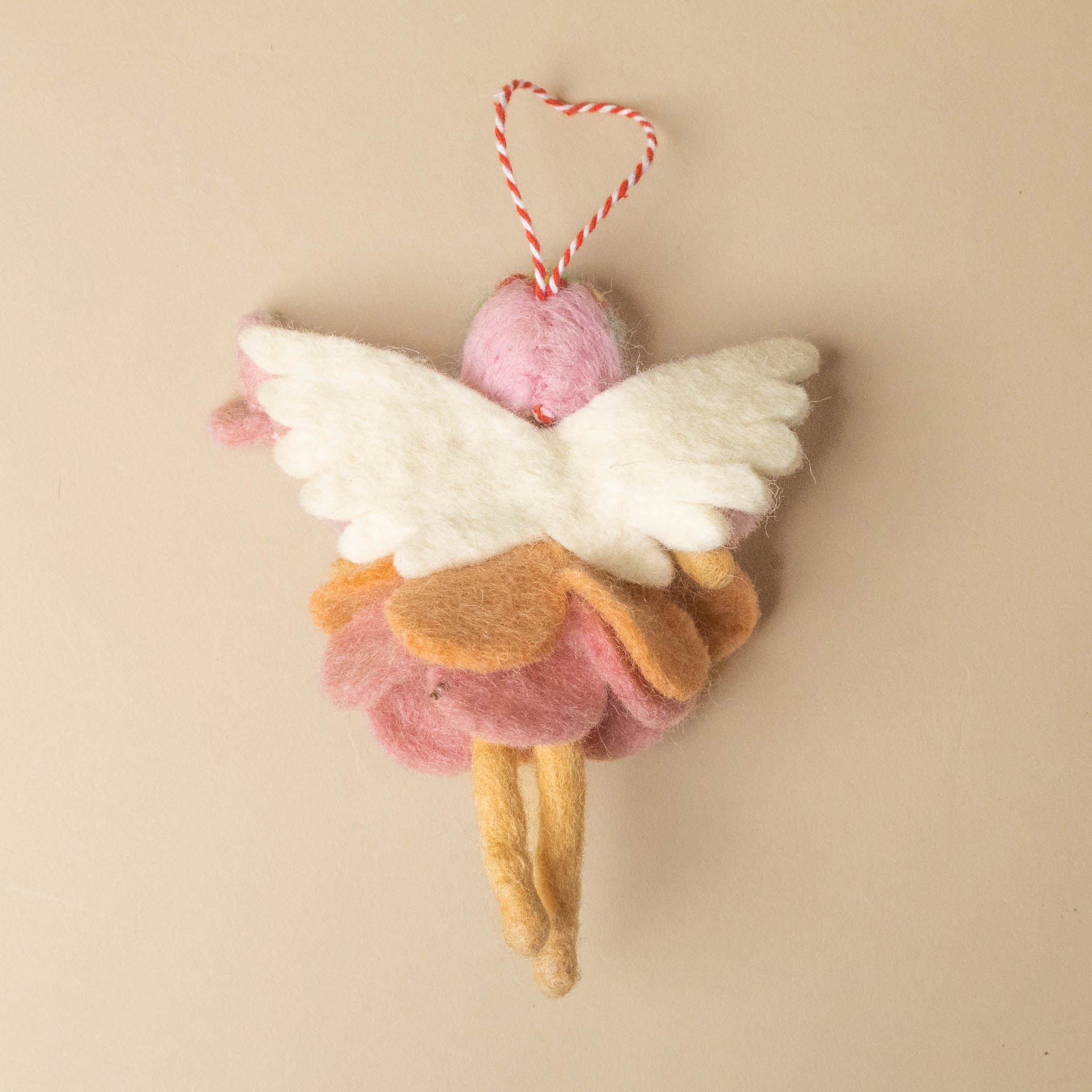 felted-garden-fairy-peachy-petal ornament with pink dress, white wings, and yellow legs on a beige background
