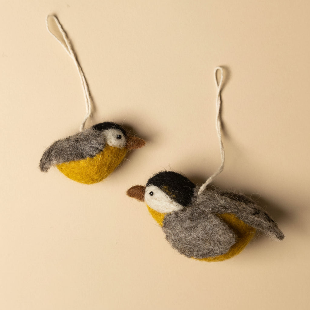 Two felted bird ornaments hanging on a beige background