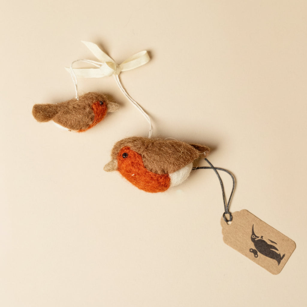 Two felted robin decorations with a tag on a beige background