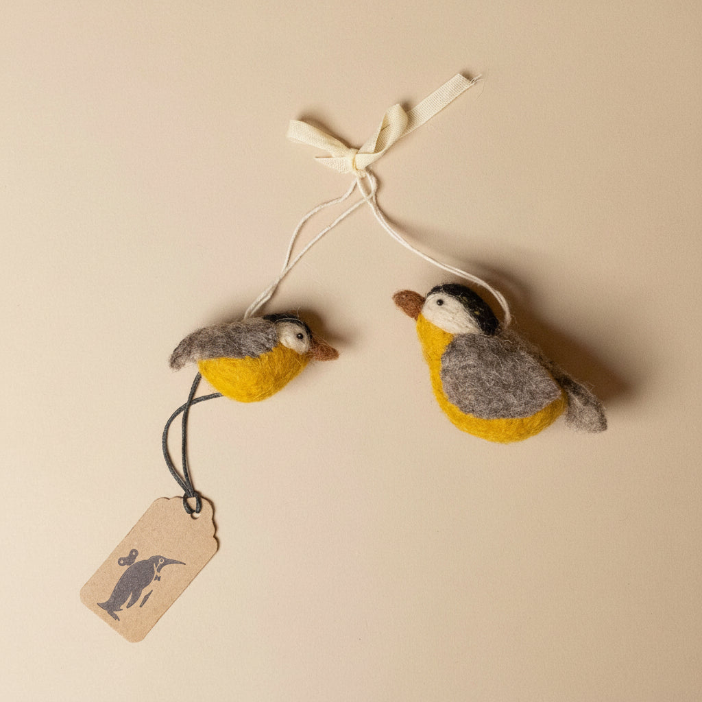 Two felted bird ornaments hanging on a string with a tag against a beige background